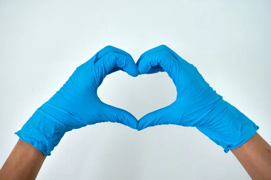 Hände in blauen Handschuhen formen ein Herz: Reinigung mit Sorgfalt